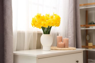 Masası, mumları ve narsisli çiçekleri olan şık bir oda.