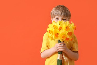 Cute little happy boy with bouquet of beautiful narcissus on orange background