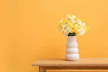 Turuncu arka planda narsist çiçekli vazo.