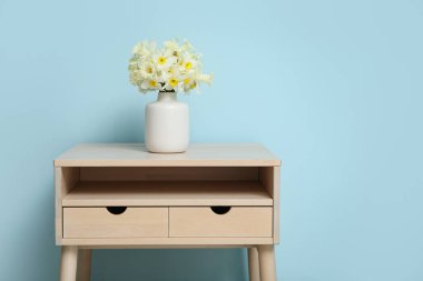 Masada mavi arka planda narsist çiçekleri olan vazo.