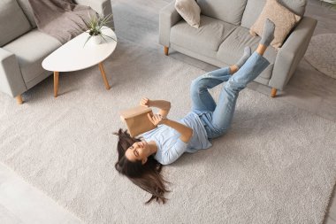 Genç ve güzel bir kadın oturma odasında yerde kitap okuyor.