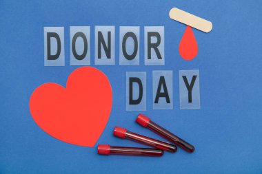 Kağıt düşüşlü kompozisyon, kalp, tıbbi yama, harf DONOR Day ve mavi arka planda test tüpleri