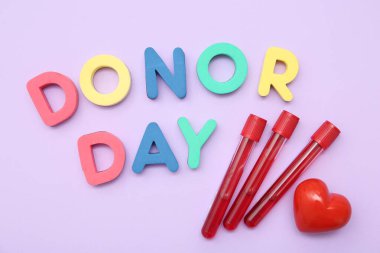 Kalp şeklinde kavrama topu, test tüpleri ve eflatun arkaplan üzerinde DONOR Day harfleri ile kompozisyon, yakın plan