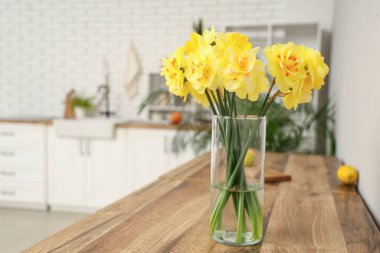 Mutfaktaki ahşap masada üzerinde bir buket nergis bulunan cam vazo.