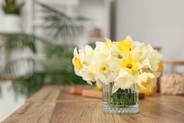 Mutfaktaki ahşap masada nergis çiçekli cam vazo, yakın plan.
