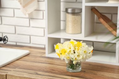 Mutfaktaki ahşap masada üzerinde bir buket nergis bulunan cam vazo.