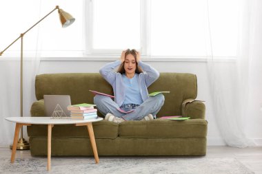 Evde kanepede oturan, elinde kitaplarla stresli bir bayan öğretmen.