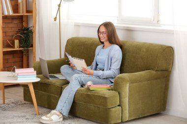 Not defterleri olan bayan öğretmen evdeki kanepede online ders veriyor.