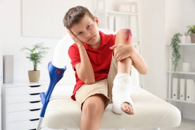 Little boy with wounded knee sitting on couch in clinic