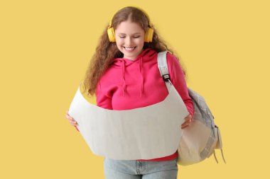 Sırt çantası, kulaklığı ve sarı arka planda posteri olan mutlu kız öğrenci.