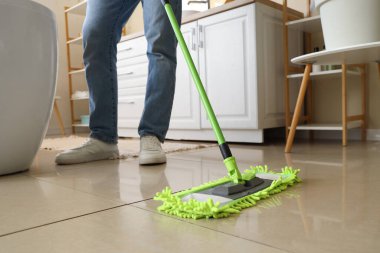 Genç adam banyoda yerleri paspaslıyor, yakın plan.