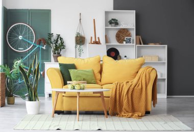 Sarı kanepeli, sehpalı, çiçekli ve bisikletli şık bir oturma odası.