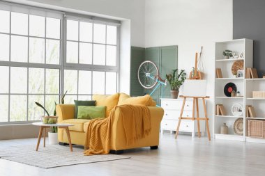 Sarı kanepeli, sehpalı, çiçekli ve bisikletli şık bir oturma odası.