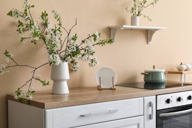 Bej mutfaktaki beyaz tezgahın üzerinde çiçek açan bir vazo.