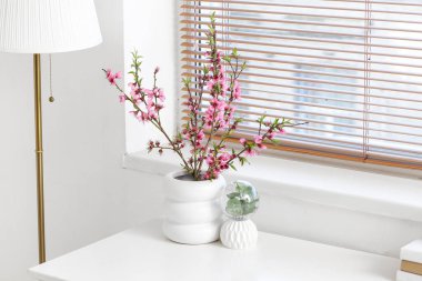 Sakura 'nın çiçek açtığı vazo beyaz odada, masanın üstünde.