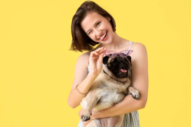 Sarı arka planda sevimli bir köpek tutan genç kadın.