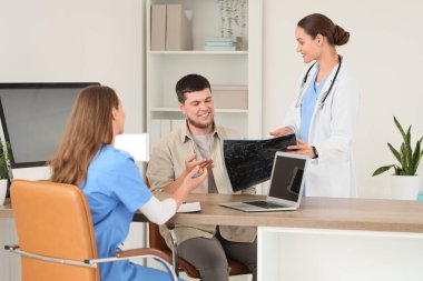 Kadın doktor, hastanede genç bir adama omurga röntgeni gösteriyor.