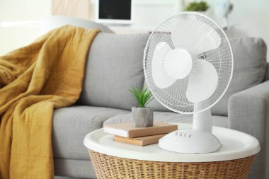Oturma odasındaki sehpanın üzerinde modern elektrikli vantilatör var.