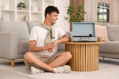 Evde müzik dinleyen pikabı olan genç bir adam.