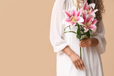 Bej arka planda pembe zambak çiçekleri olan güzel bir Afro-Amerikalı kadın.