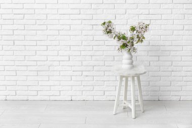 Odadaki beyaz tuğla duvarın yanındaki sehpanın üzerinde çiçek açan dalları olan vazo.