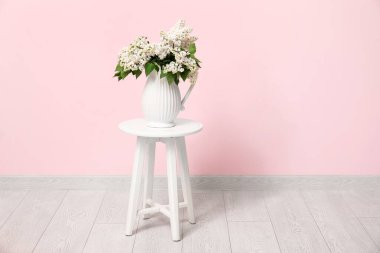 Oturma odasındaki pembe duvarın yanındaki sehpanın üzerinde leylak dalları olan vazo.