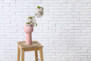 Odadaki beyaz tuğla duvarın yanındaki sehpanın üzerinde çiçek açan dalları olan vazo.