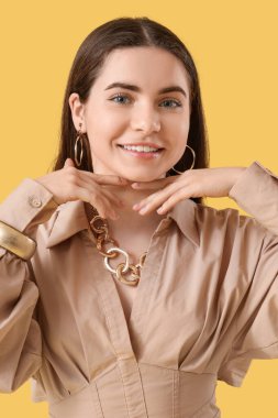 Sarı arka planda altın aksesuarları olan güzel genç bayan, yakın plan.
