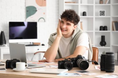 Modern kameraları ve laptopu olan profesyonel mutlu erkek fotoğrafçı stüdyoda çalışıyor.