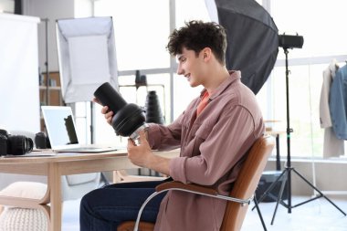 Modern kamera lensli profesyonel mutlu erkek fotoğrafçı stüdyoda sandalyede oturuyor.