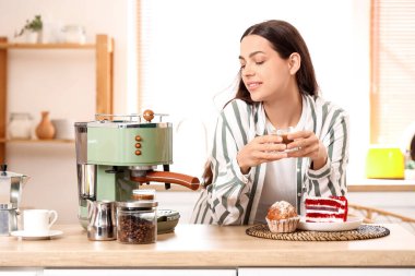 Modern kahve makinesi ve mutfaktaki tatlılarla güzel, genç ve mutlu bir kadın.