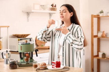 Modern kahve makinesi ve mutfaktaki tatlılarla güzel, genç ve mutlu bir kadın.