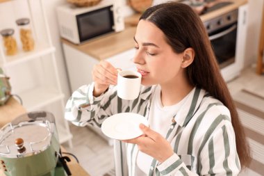 Güzel, genç, mutlu bir kadın mutfakta lezzetli bir kahve içiyor.