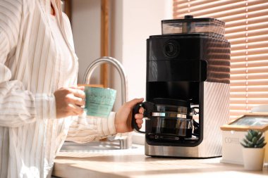 Mutfakta fincanı ve modern kahve makinesi olan güzel genç bir kadın, yakın plan.