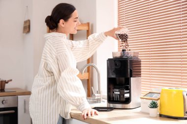 Güzel genç bir kadın, mutfakta modern bir makineyle kahve yapıyor.