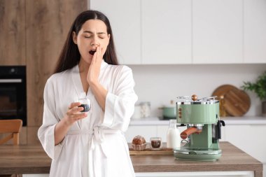 Modern kahve makinesi ve mutfakta bir fincan espresso ile güzel, genç, uykulu bir kadın.