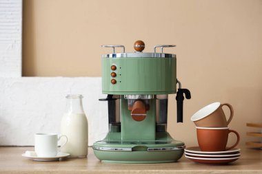 Mutfaktaki masada fincanlar ve bir şişe sütle modern kahve makinesi.