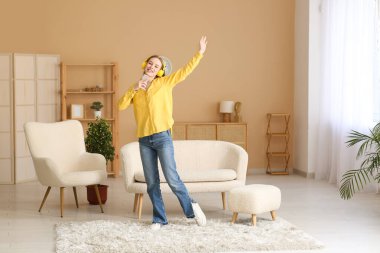 Kulaklıklı, müzik dinleyen, şık bir oturma odasında kanepede dans eden genç ve güzel bir kadın.