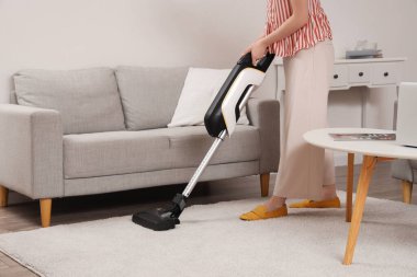 Young woman cleaning carpet with cordless stick vacuum cleaner in living room