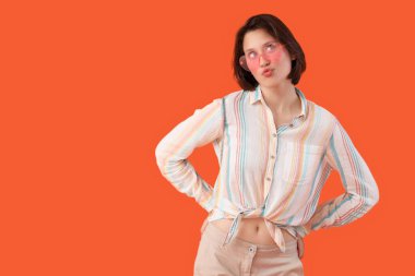 Turuncu arka planda güneş gözlüklü düşünceli genç bir kadın.