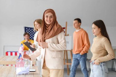 Oy sandığı yakınında oy veren Müslüman bir kadın ve oy kullanma merkezinde ABD bayrağı