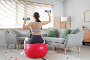 Kol halterli, spor ayakkabılı genç bir kadın evde, arkadan bakıyor.