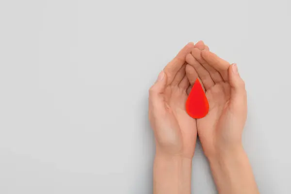 stock image Female hands with paper blood drop on grey background. Donation blood concept.