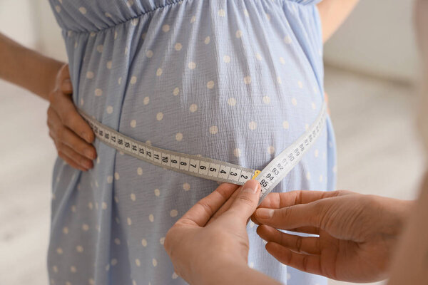 Молодая беременная женщина с дулой, измеряющей живот дома, крупным планом