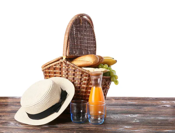 Hasır piknik sepeti, beyaz arka planda izole edilmiş kahverengi ahşap masada lezzetli yiyecekler ve bir şişe meyve suyu.