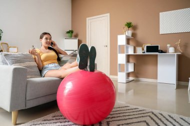 Evde kanepede cep telefonuyla konuşan genç Asyalı kadın.