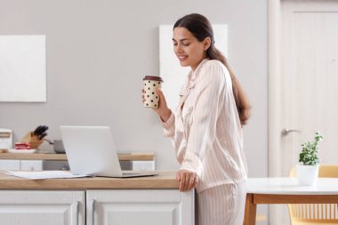 Evinde bir fincan sıcak kahve ve dizüstü bilgisayarı olan güzel bir kadın.