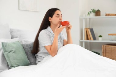Evde yatağında bir fincan sıcak kahveyle yatan güzel genç bir kadın.