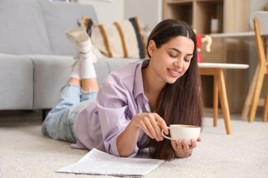 Evinde yerde yatan bir fincan sıcak kahve ve gazeteyle güzel genç bir kadın.