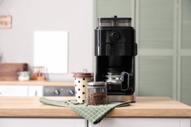 Modern kahve makinesi, fasulye ve kağıt bardak mutfaktaki ahşap masada.
